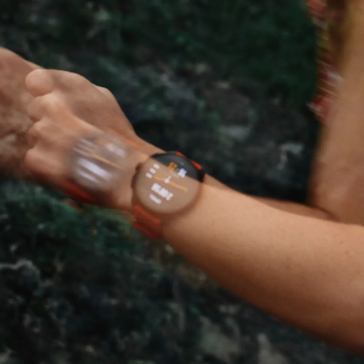A runner's forearm mid-stride, the Suunto on her wrist, moss and rock blurred behind.